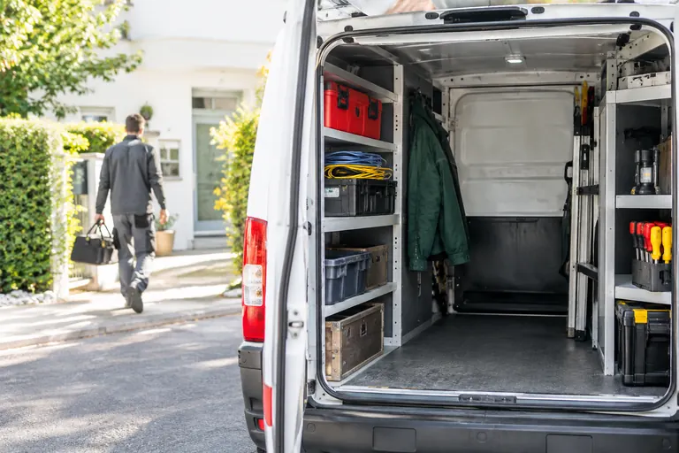 Utilitaire d’artisan ouvert avec outils rangés, garé dans une rue résidentielle calme